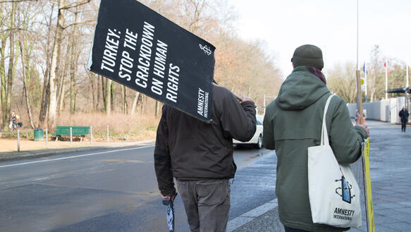 Zwei Männer laufen eine Straße entlang und tragen Amnesty-Protestschilder