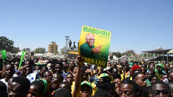 Das Foto zeigt eine Menschenmenge. Im Vordergrund hält ein Mann ein Plakat mit der Aufschrift Magafuli für den Präsidentschaftskandidaten der Regierungspartei in die Höhe.