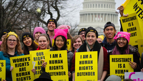Eine Gruppe junger Menschen mit Plakaten, auf denen steht: „I am a human rights defender“, dahinter ein Gebäude