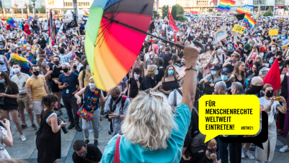 Eine Demonstration mit vielen Menschen, die Regenbogenflaggen schwenken. Im Vordergrund eine Person mit blonden Haaren von hinten, die einen Regenschirm in Regenbogenfarben in die Luft streckt. Rechts unten in der Ecke eine gelbe Sprechblase, darin steht in schwarzer Schrift: Für Menschenrechte weltweit einsetzen! #BTW21