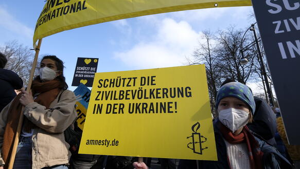Das Bild zeigt Demonstrierende mit Amnesty-Bannnern und Schildern, die den Schutz der Zivilbevölkerung in der Ukraine fordern.