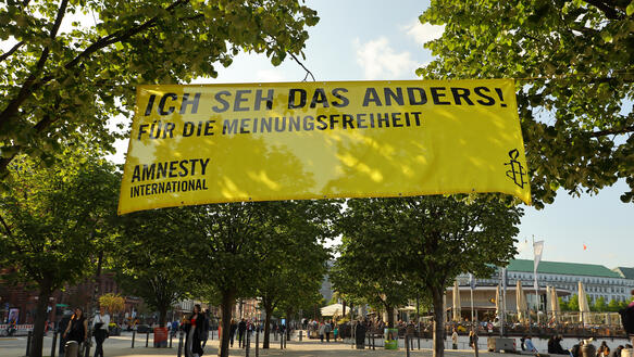 Das Bild zeigt ein Banner mit der Aufschrift "Ich seh das anders", das an Bäumen befestigt ist.