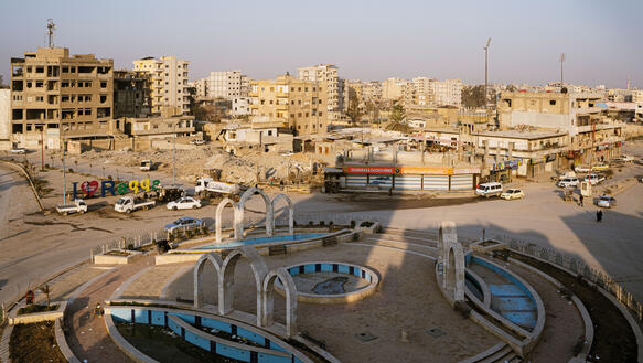 Der Naim-Platz im syrischen Rakka: ein Rondell, Kreisverkehr, darum Autos, viele zerstörte Gebäude ringsum.